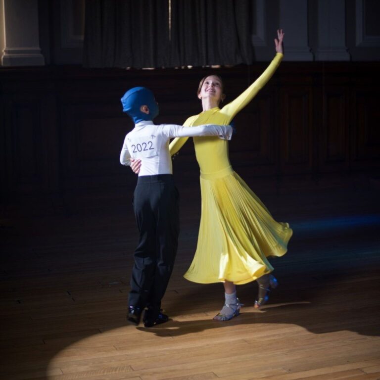 Romchyk, wearing his blue medical mask, ballroom dancing with a partner in a yellow dress