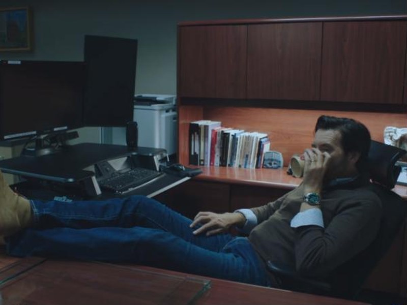 A man leans back with his feet on a desk in an office at night in Elevate